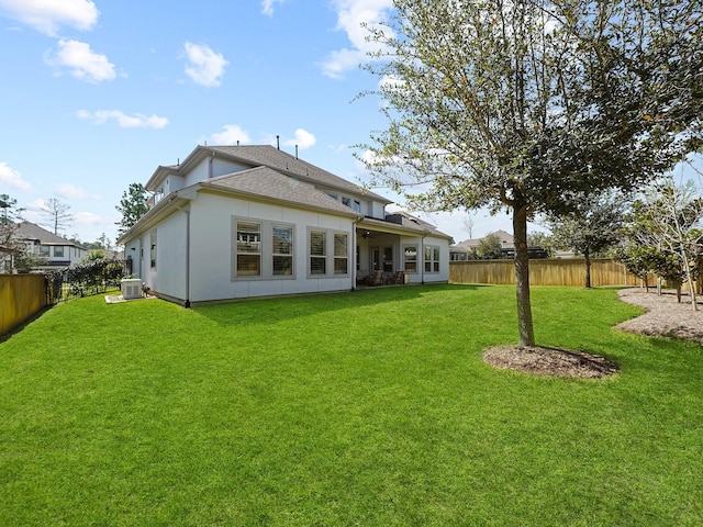 rear view of property with central AC unit, a lawn, a fenced backyard, and a shingled roof