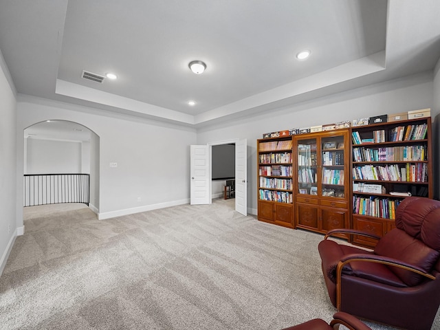 sitting room featuring arched walkways, baseboards, carpet, and a tray ceiling