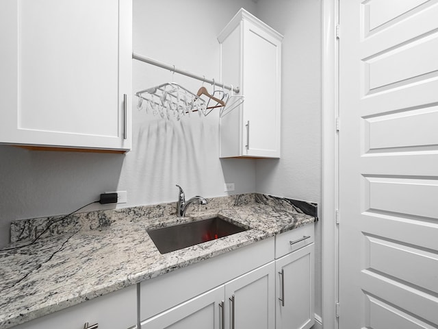 kitchen with white cabinetry, light stone countertops, and a sink