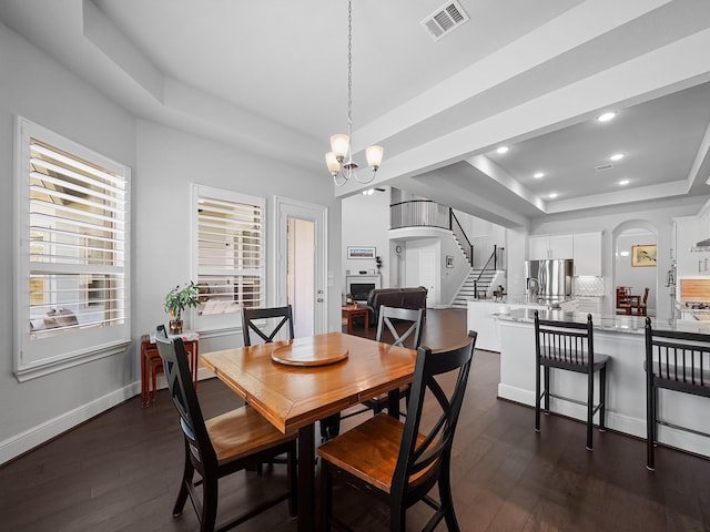 dining area featuring visible vents, dark wood finished floors, an inviting chandelier, a raised ceiling, and stairs