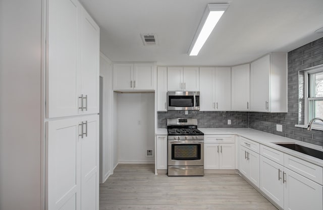 kitchen with light wood finished floors, visible vents, white cabinets, appliances with stainless steel finishes, and a sink