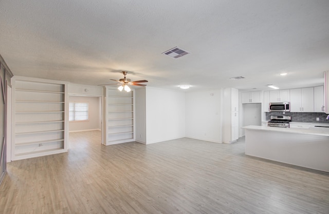 unfurnished living room featuring light wood finished floors, ceiling fan, visible vents, and a textured ceiling