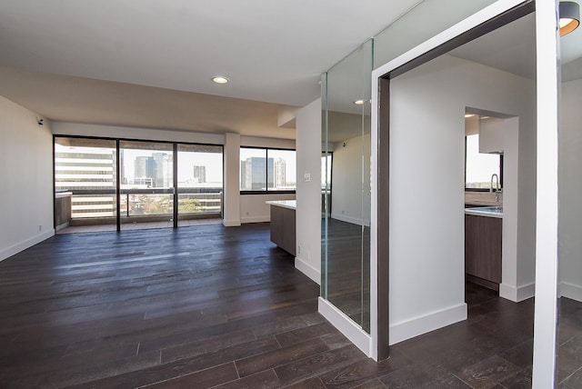 empty room with dark wood-style floors, recessed lighting, a sink, and baseboards