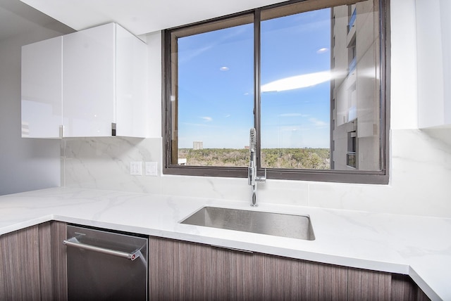 kitchen featuring light stone counters, stainless steel dishwasher, white cabinetry, a sink, and modern cabinets