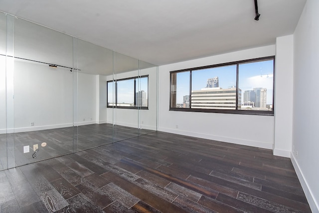 unfurnished room featuring track lighting, baseboards, a city view, and wood finished floors