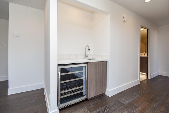 bar featuring wine cooler, a sink, dark wood finished floors, and baseboards