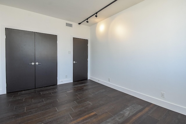 unfurnished bedroom featuring dark wood-style flooring, visible vents, baseboards, a closet, and rail lighting