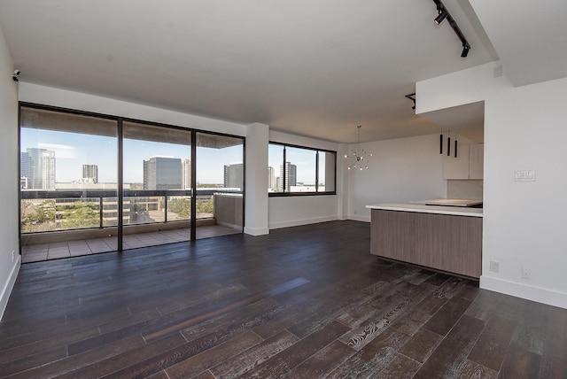 unfurnished living room with a city view, dark wood-type flooring, baseboards, rail lighting, and an inviting chandelier