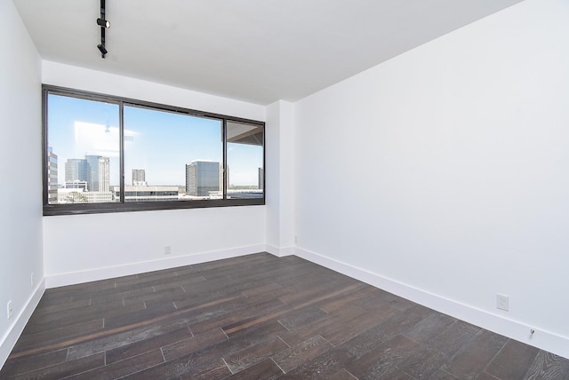 unfurnished room featuring track lighting, a city view, dark wood finished floors, and baseboards