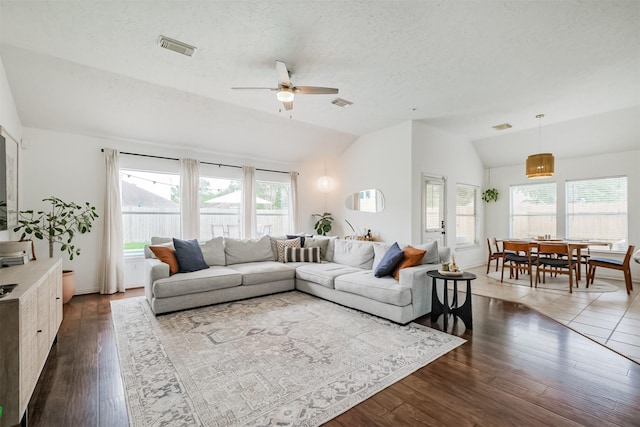 living area featuring vaulted ceiling, dark wood-style flooring, plenty of natural light, and visible vents