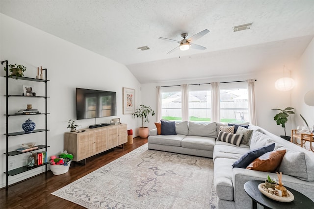 living room with dark wood-style flooring, lofted ceiling, visible vents, ceiling fan, and a textured ceiling