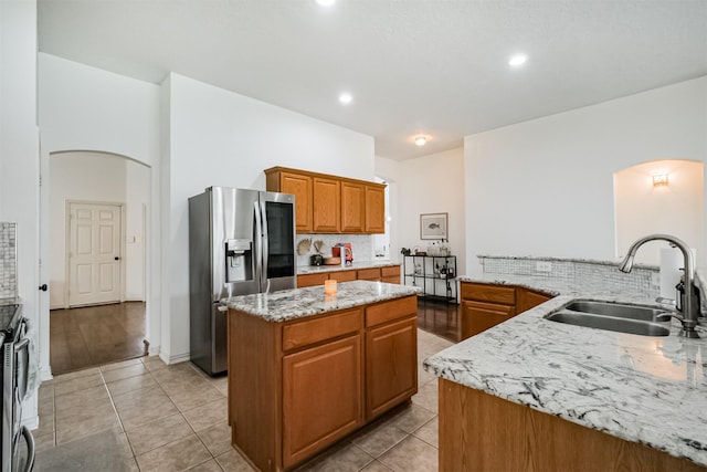 kitchen featuring tasteful backsplash, arched walkways, a center island, stainless steel appliances, and a sink