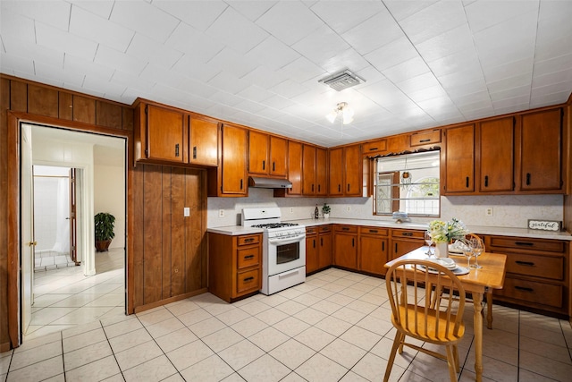 kitchen with light countertops, white range with gas stovetop, brown cabinets, and wood walls