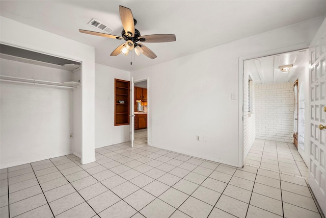 unfurnished bedroom with light tile patterned floors, visible vents, brick wall, ceiling fan, and a closet