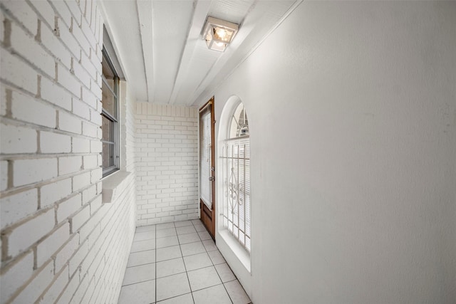 corridor with light tile patterned floors and brick wall