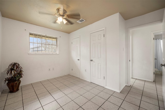 unfurnished bedroom with multiple closets, light tile patterned flooring, visible vents, and a ceiling fan