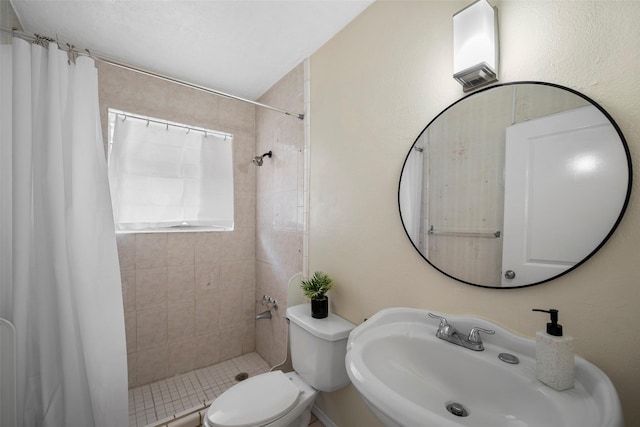 full bathroom featuring a textured wall, tiled shower, a sink, and toilet