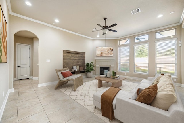 living area with light tile patterned floors, visible vents, arched walkways, a glass covered fireplace, and ornamental molding