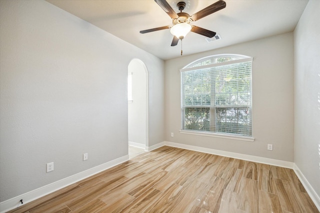 unfurnished room with arched walkways, visible vents, baseboards, and wood finished floors