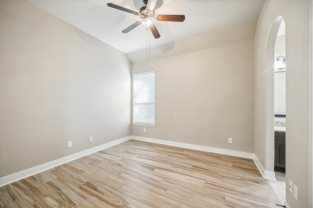 spare room with ceiling fan, light wood-style flooring, baseboards, and arched walkways