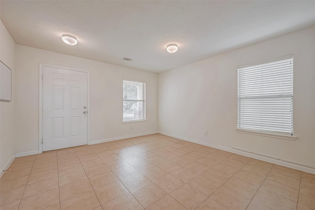 empty room with baseboards, visible vents, a textured ceiling, and light tile patterned flooring