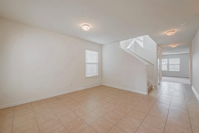 spare room featuring baseboards, stairway, and a healthy amount of sunlight