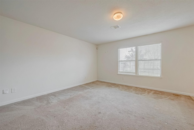 unfurnished room with baseboards, a textured ceiling, visible vents, and light colored carpet