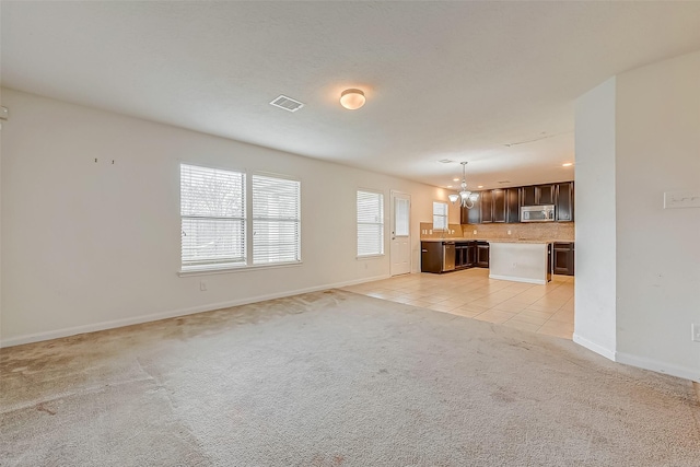 unfurnished living room with light tile patterned flooring, light carpet, visible vents, baseboards, and an inviting chandelier