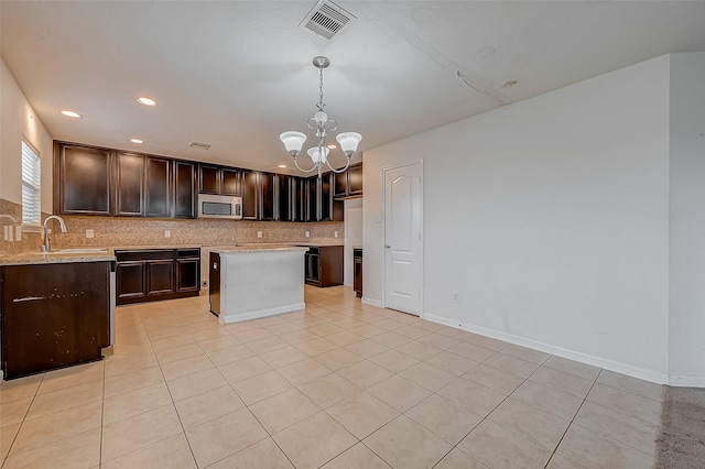 kitchen with stainless steel microwave, backsplash, a sink, dark brown cabinets, and a notable chandelier