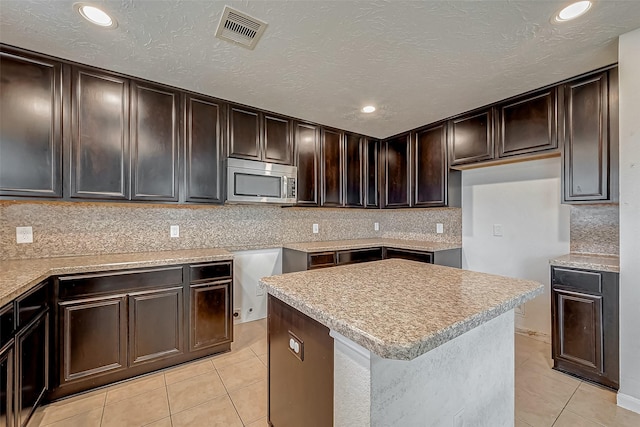 kitchen with light tile patterned flooring, visible vents, dark brown cabinets, tasteful backsplash, and stainless steel microwave