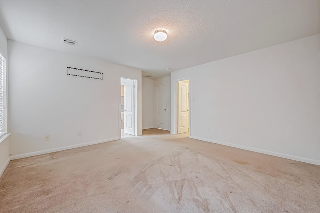 unfurnished room featuring light colored carpet, visible vents, a textured ceiling, and baseboards