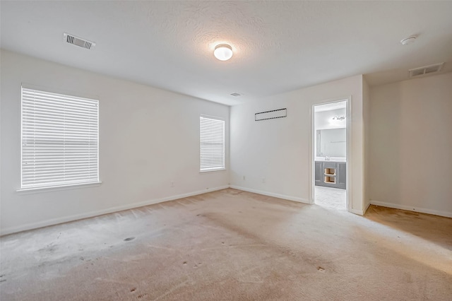 spare room with carpet flooring, visible vents, a textured ceiling, and baseboards