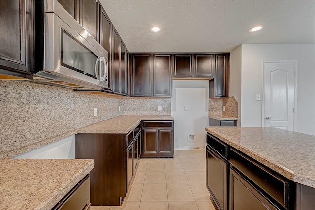 kitchen with light tile patterned floors, stainless steel microwave, dark brown cabinets, backsplash, and recessed lighting