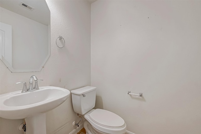 half bathroom featuring visible vents, a sink, toilet, and baseboards