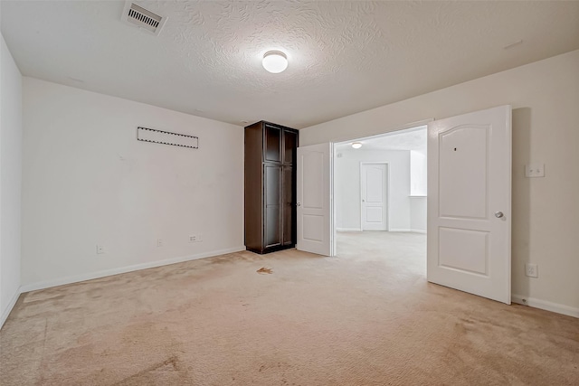 spare room with baseboards, visible vents, a textured ceiling, and light colored carpet