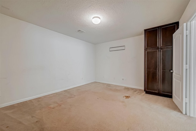 unfurnished bedroom featuring baseboards, visible vents, a textured ceiling, and light colored carpet