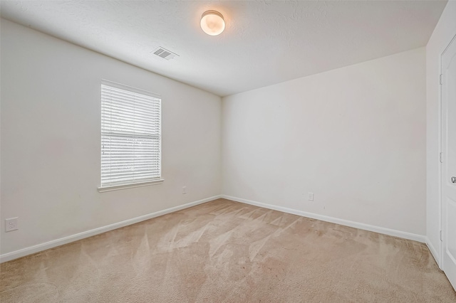 empty room featuring light colored carpet, visible vents, a textured ceiling, and baseboards