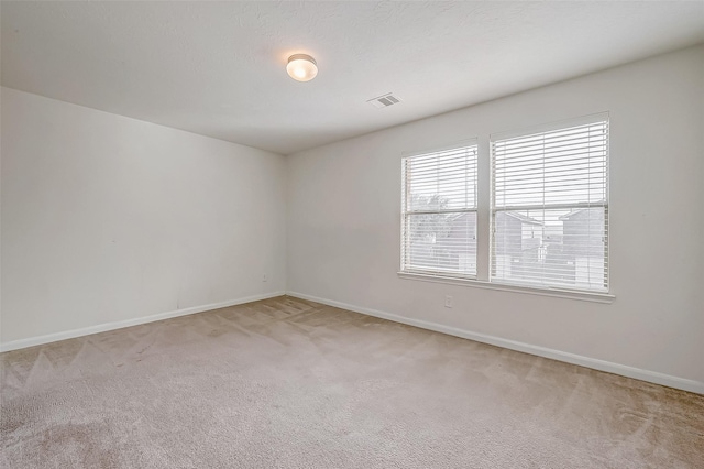 empty room featuring light carpet, visible vents, and baseboards