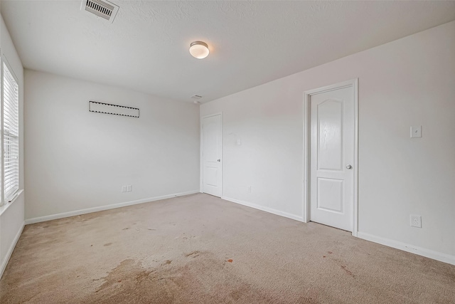 carpeted empty room with visible vents, a textured ceiling, and baseboards