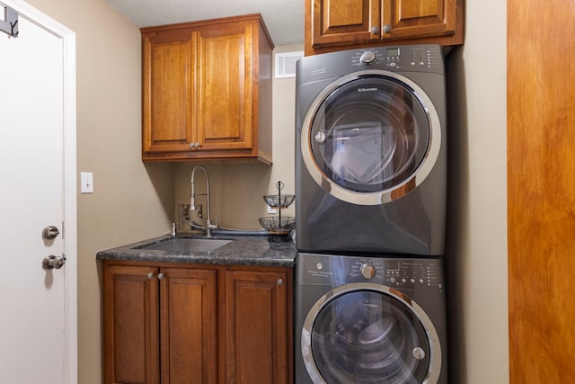 clothes washing area featuring cabinet space, visible vents, a sink, a textured ceiling, and stacked washing maching and dryer