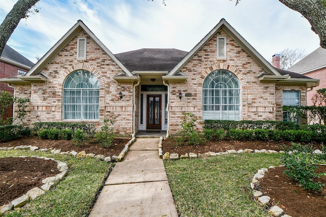 view of front of home featuring brick siding and roof with shingles