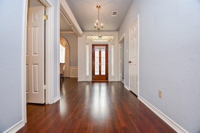 foyer entrance featuring dark wood-style floors, baseboards, visible vents, a textured wall, and a chandelier