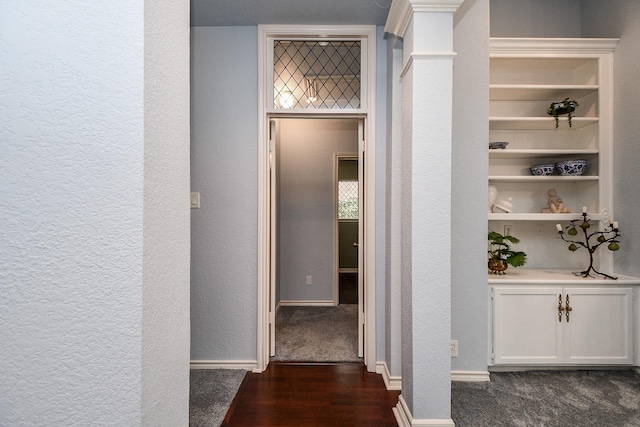 corridor featuring a textured wall, baseboards, ornate columns, and dark wood-style flooring