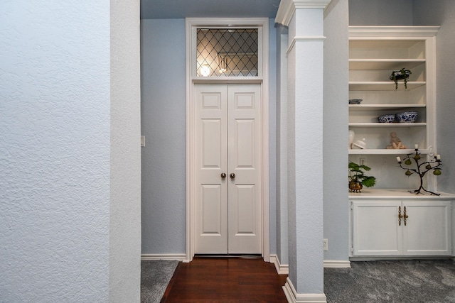 interior space featuring built in features, baseboards, decorative columns, dark wood-style flooring, and a textured wall