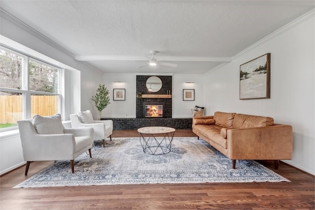 living area with a textured ceiling, ornamental molding, a brick fireplace, wood finished floors, and a ceiling fan