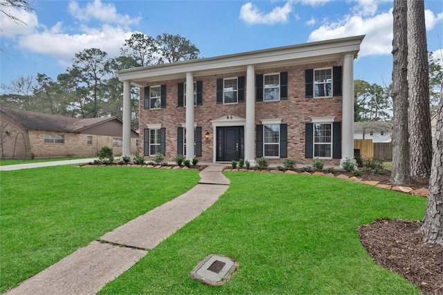 greek revival inspired property with brick siding, fence, and a front yard