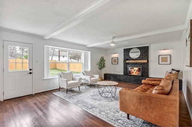 living room with a textured ceiling, beamed ceiling, a brick fireplace, wood finished floors, and a ceiling fan