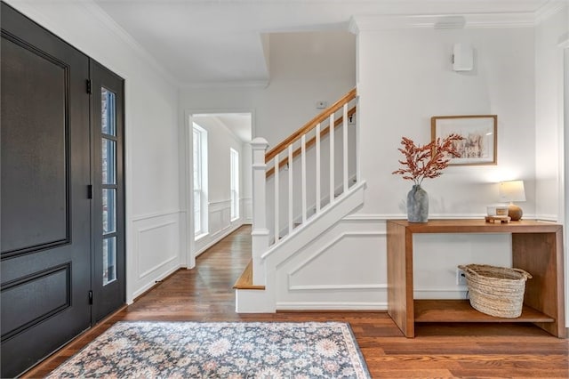 entryway with ornamental molding, stairway, wood finished floors, and a decorative wall