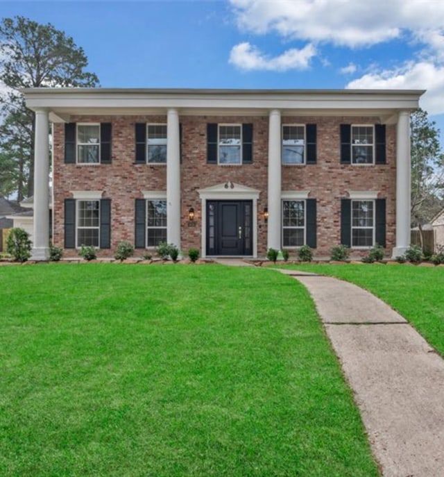 greek revival inspired property featuring brick siding and a front yard