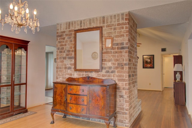 hall with vaulted ceiling, a textured ceiling, wood finished floors, and visible vents